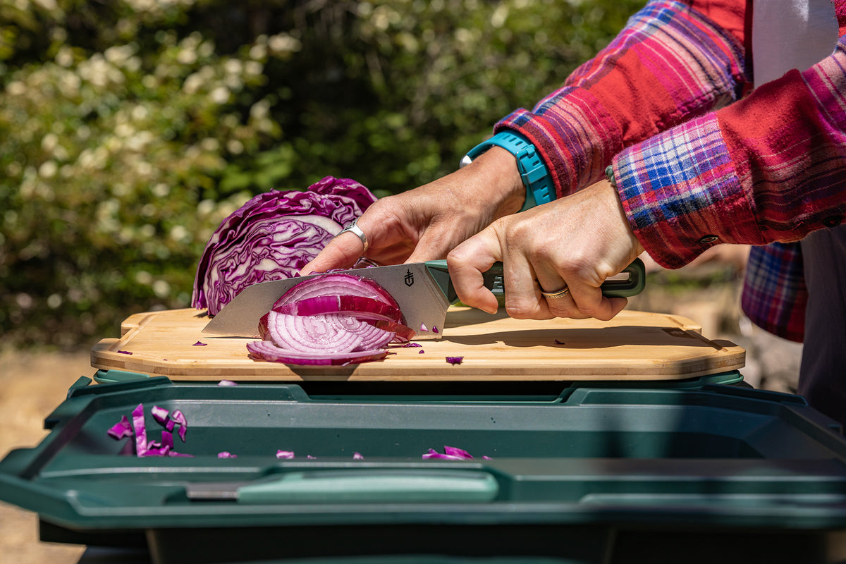 A person wearing a red and blue plaid shirt slices a purple red cabbage on ComplEAT Cutting Board Set.