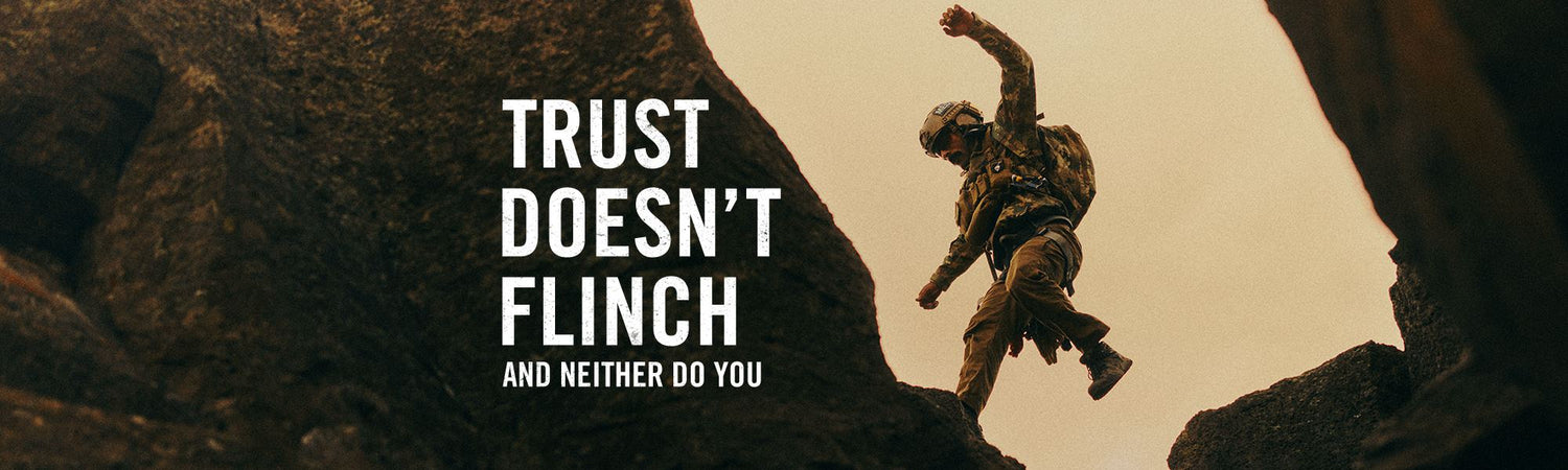 A climber scaling a rocky outcrop against a warm beige sky, with bold white text reading 'TRUST DOESN'T FLINCH AND NEITHER DO YOU' on the left side.